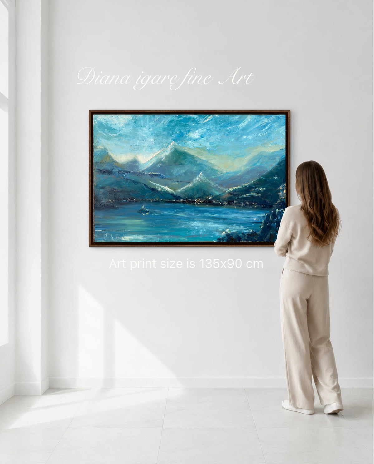 A woman in a beige tracksuit stands with her back to a framed landscape painting of blue mountains and a lake, mounted on a white wall. White text overlays read 'Diana igare fine Art' and 'Art print size is 135x90 cm'.