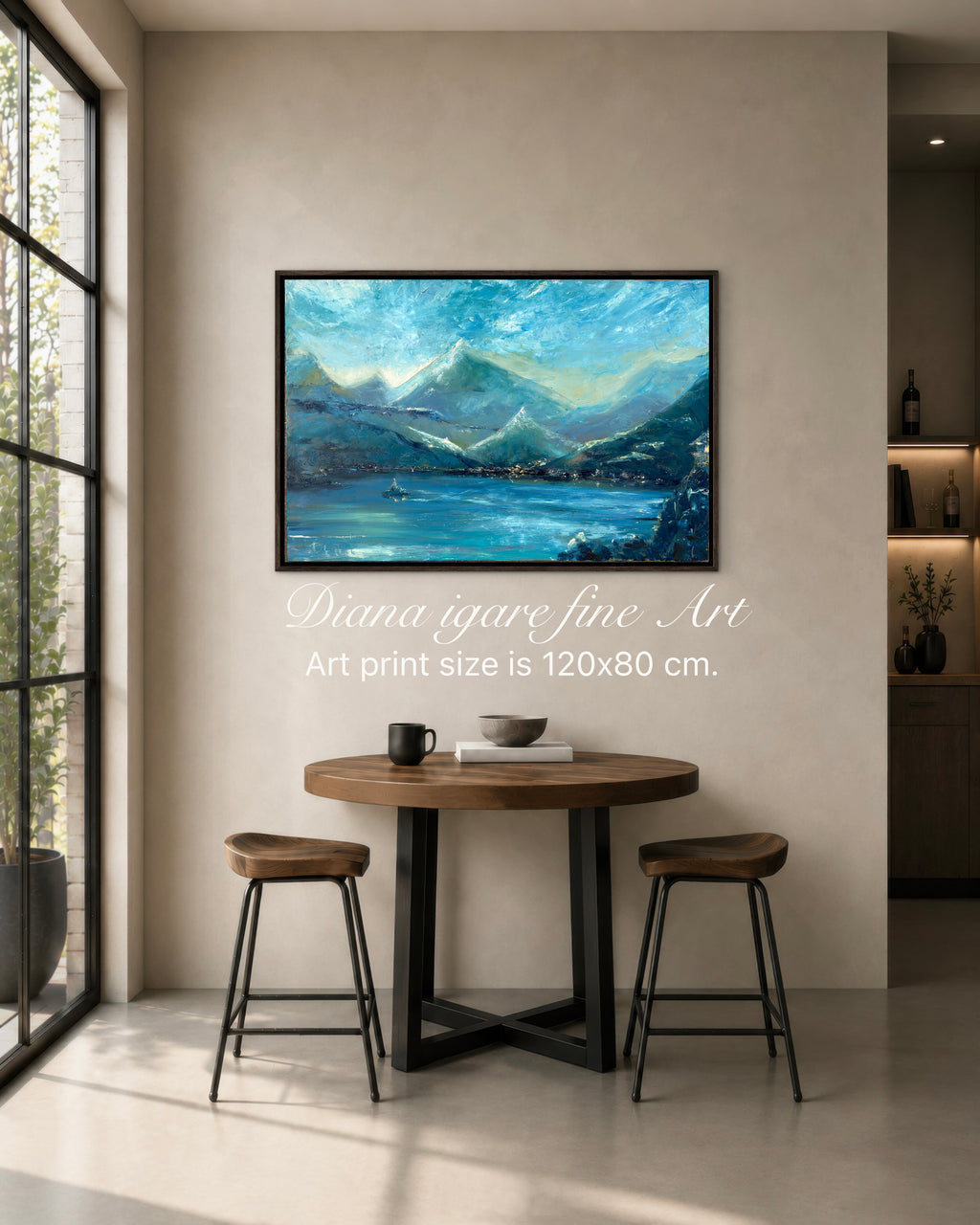 A framed landscape art print depicting blue mountains and a lake, displayed on a beige wall in a modern dining room setting with a wooden table and two stools. White text overlay reads 'Diana igare fine Art Art print size is 120x80 cm.