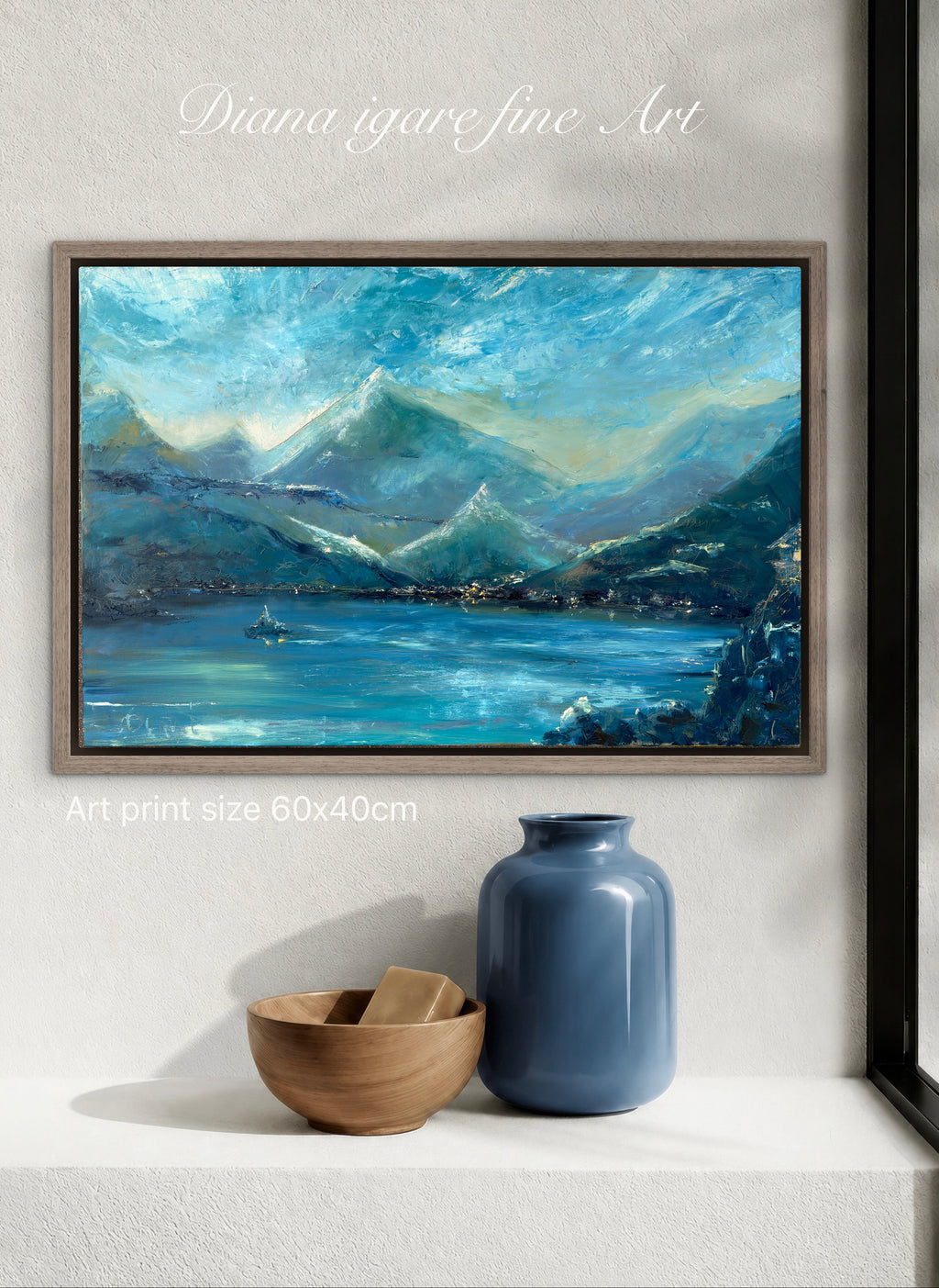 A framed landscape painting of blue mountains and a lake, displayed on a white wall above a shelf with a blue vase and a wooden bowl. Text overlays read 'Diana igare fine Art' and 'Art print size 60x40cm'.